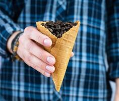 The barista girl holds a waffle glass with fragrant coffee beans. Natural coffee. Close-up. Selective focus. photo