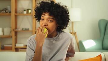 gelukkig mooi meisje bijten groen appel Bij huis. mooi Afrikaanse Amerikaans jong vrouw aan het eten vers fruit en lachend. gezond voedsel veganistisch vegetarisch dieet concept. gezond tussendoortje schoon voedsel video