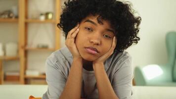 African american sad thoughtful pensive unmotivated girl sitting on sofa at home indoor. Young african woman ponder look tired after long day. Girl feels depressed offended lonely upset heartbreak video