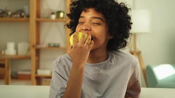 glücklich ziemlich Mädchen beißen Grün Apfel beim heim. schön afrikanisch amerikanisch jung Frau Essen frisch Obst und lächelnd. gesund Essen vegan Vegetarier Diät Konzept. gesund Snack sauber Essen video