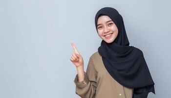 young muslim in hijab pointing one side in studio isolated plain gray background photo