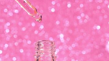 macro glass pipette with liquid fluid oil or serum drops on pink bokeh background, cosmetic liquid skin care product video