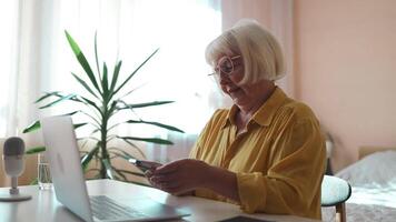 60s företag kvinna professionell användare arbetstagare använder sig av skriver på telefon sitta på Hem kontor skrivbord arbetssätt uppkopplad med pc programvara appar teknologi begrepp, stänga upp sida se video