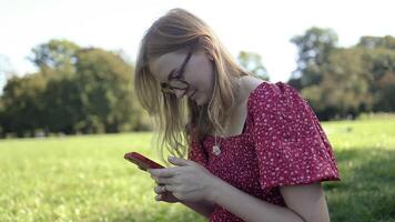 detailopname van een Kaukasisch vrouw chatten met haar vrienden door haar smartphone, gebruik makend van haar telefoon terwijl ontspannende in de achtertuin Bij zomer park video