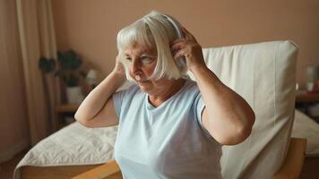 Close up sleepy peaceful mature woman with headphones enjoy quality sound relaxing alone at home and listening to music video