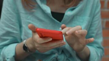 de cerca Disparo de caucásico mujer en acogedor ropa utilizando su teléfono inteligente, chateando con alguien o desplazamiento en su teléfono mientras relajante a un cafetería. video