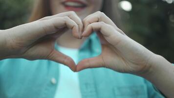 Closeup of smiling pretty Caucasian woman confesses in love, makes heart gesture, shows her true feelings, has happy expression video