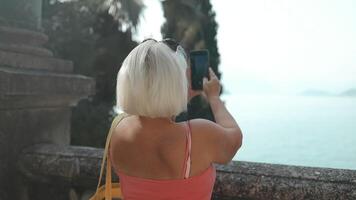 espalda vista. mujer fotógrafo tomando foto de montañas y azul lago de como en Italia. viaje y pasatiempo concepto video