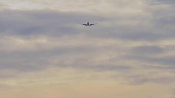 Jet plane approaching landing. Passenger airliner flies in the cloudy sunset sky, front view, long shot. Cinematic footage of aviation. Background crimson sky video