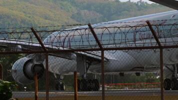 PHUKET, THAILAND - JANUARY 26, 2023. Airbus A330-302, A7-AEO of Qatar Airways taxiing to the runway at Phuket airport. Board behind the airport fence, side view, medium shot video