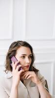 Contemplative Millennial Woman Engages in a Phone Call, Converses Thoughtfully, Reflecting While Seated on a Chair photo