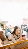 Joyful Millennial Woman Relaxing on Sofa, Engrossed in Phone Messages, Chatting, and Enjoying Leisure Time. Content and Carefree Young Female Lounging on Couch Embracing Digital Communication at Home. photo