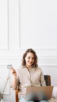 Joyful Millennial Woman Typing on Laptop, Seamlessly Using Credit Card for Online Shopping, Creating a Modern Image of Convenience and Enjoyment in Digital Retail Experience at Home photo