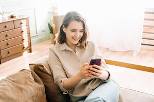 Digital Connection Delight. Happy millennial woman in wireless headphones looks at phone, reads messages, enjoys chatting. Modern Communication, Technology Bliss, and Joyful Digital Lifestyle Concept. photo