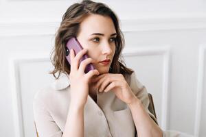 contemplativo milenario mujer se involucra en un teléfono llamar, conversa pensativamente, reflejando mientras sentado en un silla foto