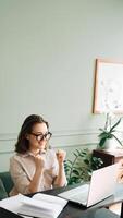 Victory and Joy. Smiling Woman Gesturing in Successful Laptop Video Chat. Triumphant Video Call. Joyful Woman in Glasses Beams as She Communicates on Laptop, Signaling Victory and Success photo