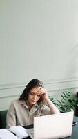 sobrecargado de trabajo y estresado. joven mujer siesta a computadora portátil, perdido en pensamientos. agotado y estresado. joven mujer contemplando a computadora portátil, abrumado por trabajo excesivo y fatiga foto