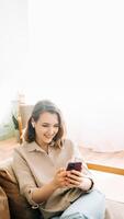 Digital Connection Delight. Happy millennial woman in wireless headphones looks at phone, reads messages, enjoys chatting. Modern Communication, Technology Bliss, and Joyful Digital Lifestyle Concept. photo