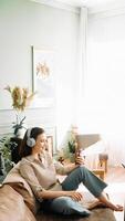 alegre conectividad. joven mujer en inalámbrico auriculares, sonriente como ella se involucra en un en línea llamada en su teléfono inteligente foto