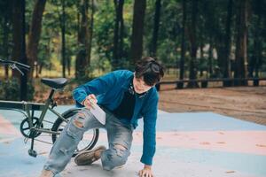 joven hermoso barbado hombre tomando un descanso mientras de viaje el ciudad con su bicicleta utilizando su digital tableta mirando lejos pensativamente foto