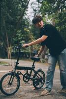 joven hermoso barbado hombre tomando un descanso mientras de viaje el ciudad con su bicicleta utilizando su digital tableta mirando lejos pensativamente foto