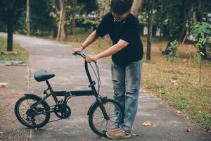 joven hermoso barbado hombre tomando un descanso mientras de viaje el ciudad con su bicicleta utilizando su digital tableta mirando lejos pensativamente foto