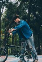 Young handsome bearded man taking a break while travelling the city with his bicycle using his digital tablet looking away thoughtfully photo