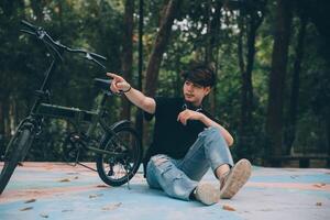 Young handsome bearded man taking a break while travelling the city with his bicycle using his digital tablet looking away thoughtfully photo