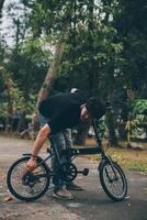 joven hermoso barbado hombre tomando un descanso mientras de viaje el ciudad con su bicicleta utilizando su digital tableta mirando lejos pensativamente foto