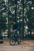 joven hermoso barbado hombre tomando un descanso mientras de viaje el ciudad con su bicicleta utilizando su digital tableta mirando lejos pensativamente foto
