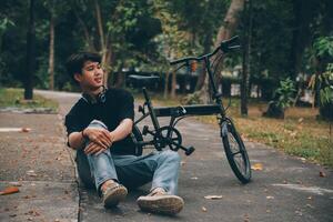 joven hermoso barbado hombre tomando un descanso mientras de viaje el ciudad con su bicicleta utilizando su digital tableta mirando lejos pensativamente foto