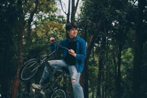 joven hermoso barbado hombre tomando un descanso mientras de viaje el ciudad con su bicicleta utilizando su digital tableta mirando lejos pensativamente foto