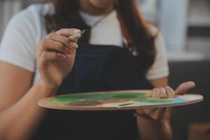 Cropped image of female artist standing in front of an easel and dipping brush into color palette photo