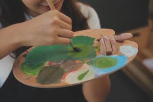 Cropped image of female artist standing in front of an easel and dipping brush into color palette photo