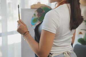 Cropped image of female artist standing in front of an easel and dipping brush into color palette photo