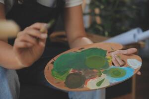 Cropped image of female artist standing in front of an easel and dipping brush into color palette photo