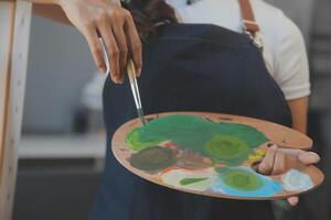 Cropped image of female artist standing in front of an easel and dipping brush into color palette photo