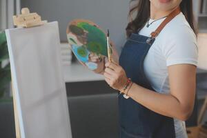 Cropped image of female artist standing in front of an easel and dipping brush into color palette photo