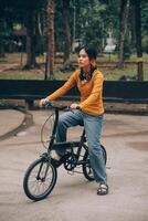 Happy young Asian woman while riding a bicycle in a city park. She smiled using the bicycle of transportation. Environmentally friendly concept. photo