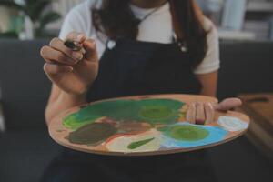 Cropped image of female artist standing in front of an easel and dipping brush into color palette photo