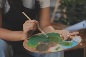 Cropped image of female artist standing in front of an easel and dipping brush into color palette photo