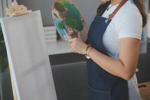 Cropped image of female artist standing in front of an easel and dipping brush into color palette photo