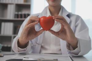 manos de médico mujer participación rojo corazón, demostración símbolo de amar, humano apoyo a paciente, promoviendo médico seguro, temprano chequeo para cuidado de la salud, cardiólogo ayuda. cerca arriba de objeto foto