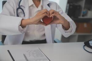 manos de médico mujer participación rojo corazón, demostración símbolo de amar, humano apoyo a paciente, promoviendo médico seguro, temprano chequeo para cuidado de la salud, cardiólogo ayuda. cerca arriba de objeto foto