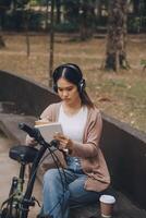 Happy young Asian woman while riding a bicycle in a city park. She smiled using the bicycle of transportation. Environmentally friendly concept. photo