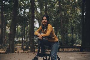 Happy young Asian woman while riding a bicycle in a city park. She smiled using the bicycle of transportation. Environmentally friendly concept. photo