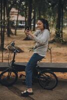 contento asiático joven mujer caminar y paseo bicicleta en parque, calle ciudad su sonriente utilizando bicicleta de transporte, eco amigable, personas estilo de vida concepto. foto