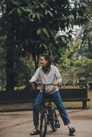 contento asiático joven mujer caminar y paseo bicicleta en parque, calle ciudad su sonriente utilizando bicicleta de transporte, eco amigable, personas estilo de vida concepto. foto