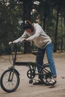 contento asiático joven mujer caminar y paseo bicicleta en parque, calle ciudad su sonriente utilizando bicicleta de transporte, eco amigable, personas estilo de vida concepto. foto