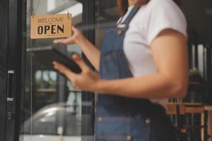 Startup successful small business owner sme beauty girl stand with tablet smartphone in coffee shop restaurant. Portrait of asian tan woman barista cafe owner. SME entrepreneur seller business concept photo